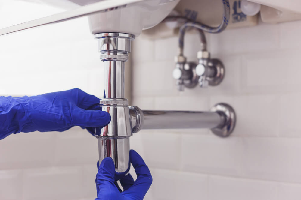 Plumber repairs and maintains chrome siphon under the washbasin